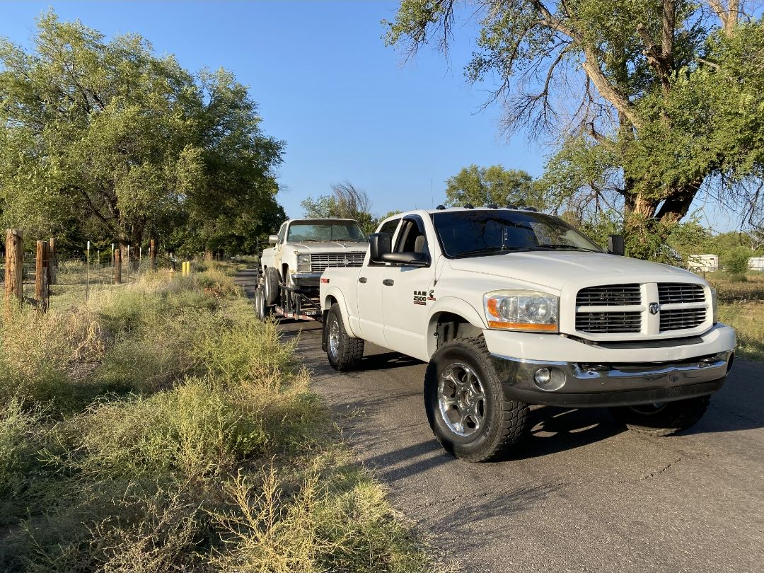 White Dodge Ram pulling a flatbed trailer loaded with a pickup