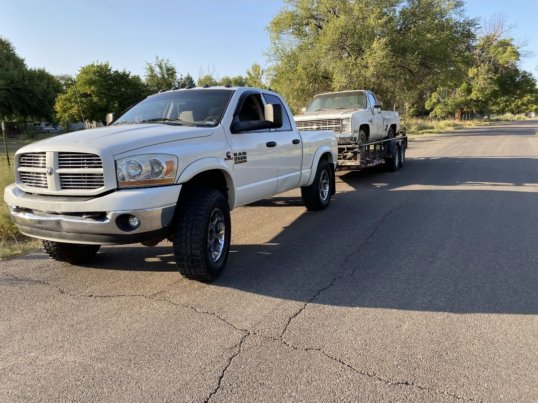 White Dodge Ram towing a pickup on a flatbed trailer down a street