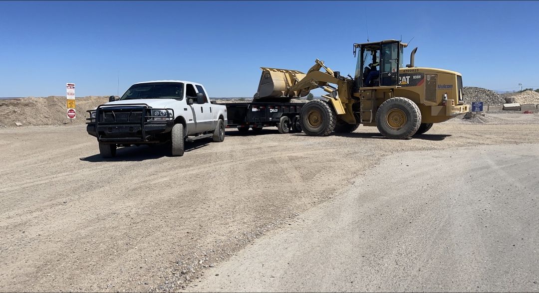 White Ford F-250, black dump trailer and wheel loader at a materials yard